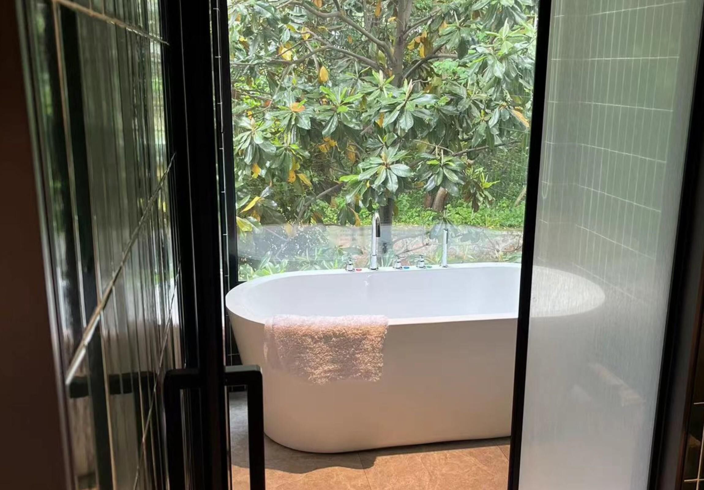 Un baño moderno con una bañera independiente, cabina de ducha de vidrio y vistas a exuberante vegetación.