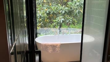 Un baño moderno con una bañera independiente, cabina de ducha de vidrio y vistas a exuberante vegetación.