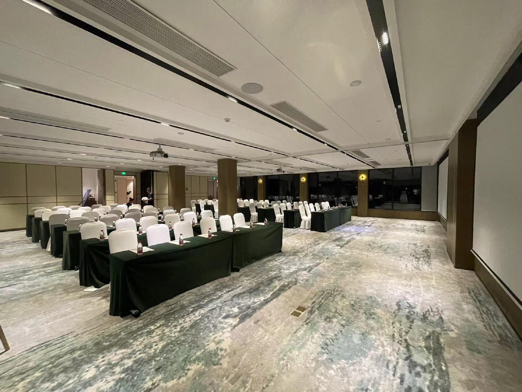 A conference room with rows of white chairs and tables, equipped with projectors and speakers, in a modern hotel setting.
