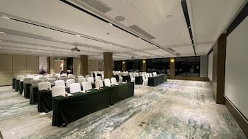A conference room with rows of white chairs and tables, equipped with projectors and speakers, in a modern hotel setting.