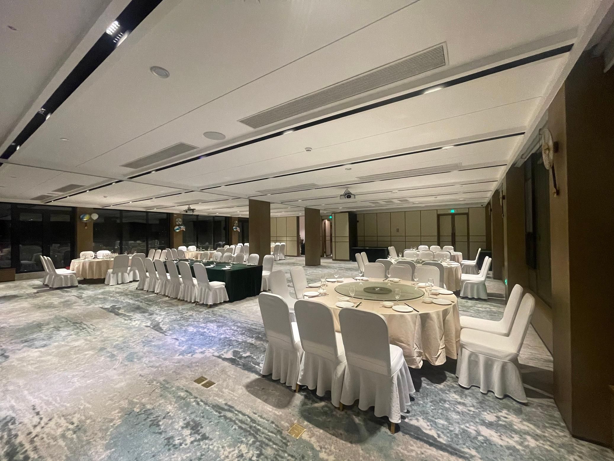Un salón de conferencias con mesas redondas y sillas blancas, ventanas amplias y suelo de mármol.