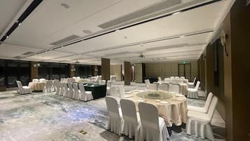 Un salón de conferencias con mesas redondas y sillas blancas, ventanas amplias y suelo de mármol.
