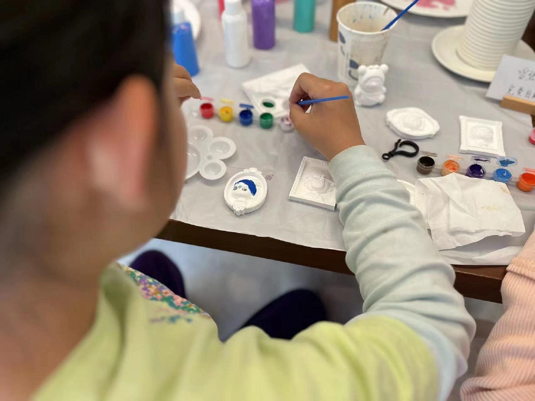 A person painting on a white surface with various paint colors and brushes.