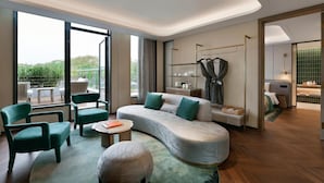A modern hotel room with a curved sofa, green armchairs, a small round table, and a view of greenery outside. - Blossom Hill Hotel Nanjing Bojin (Nanjing)