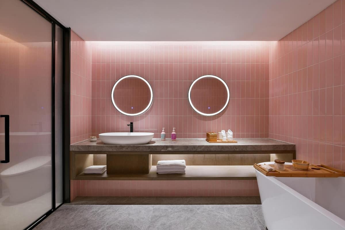 Ein modernes Badezimmer mit einem großen Waschbecken, zwei runden Spiegeln und rosafarben gefliesten Wänden.