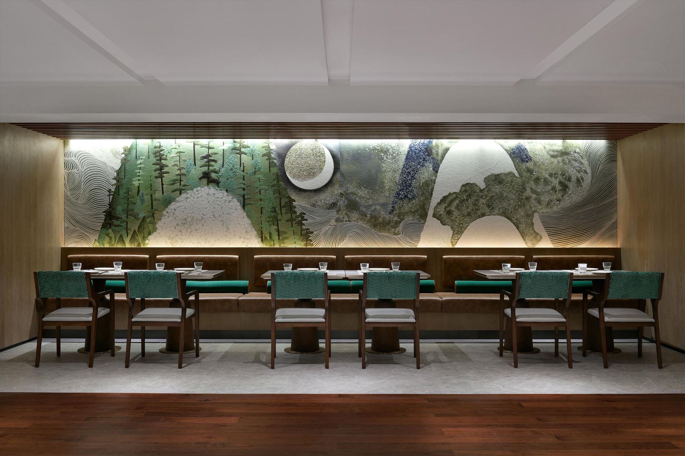 Un restaurante con una barra larga, cabinas tapizadas de verde y un mural grande en la pared.