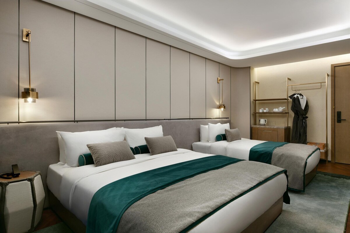 A hotel room with two beds, a bedside table, a wardrobe, and a mirror.