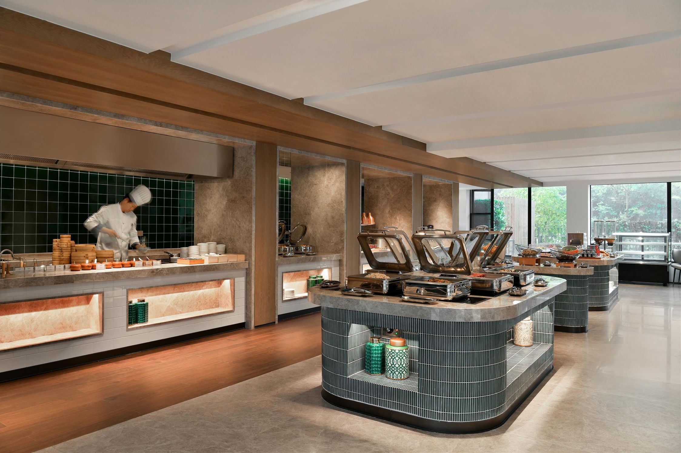 A modern kitchen with a chef preparing food, large windows, and a clean, organized layout.