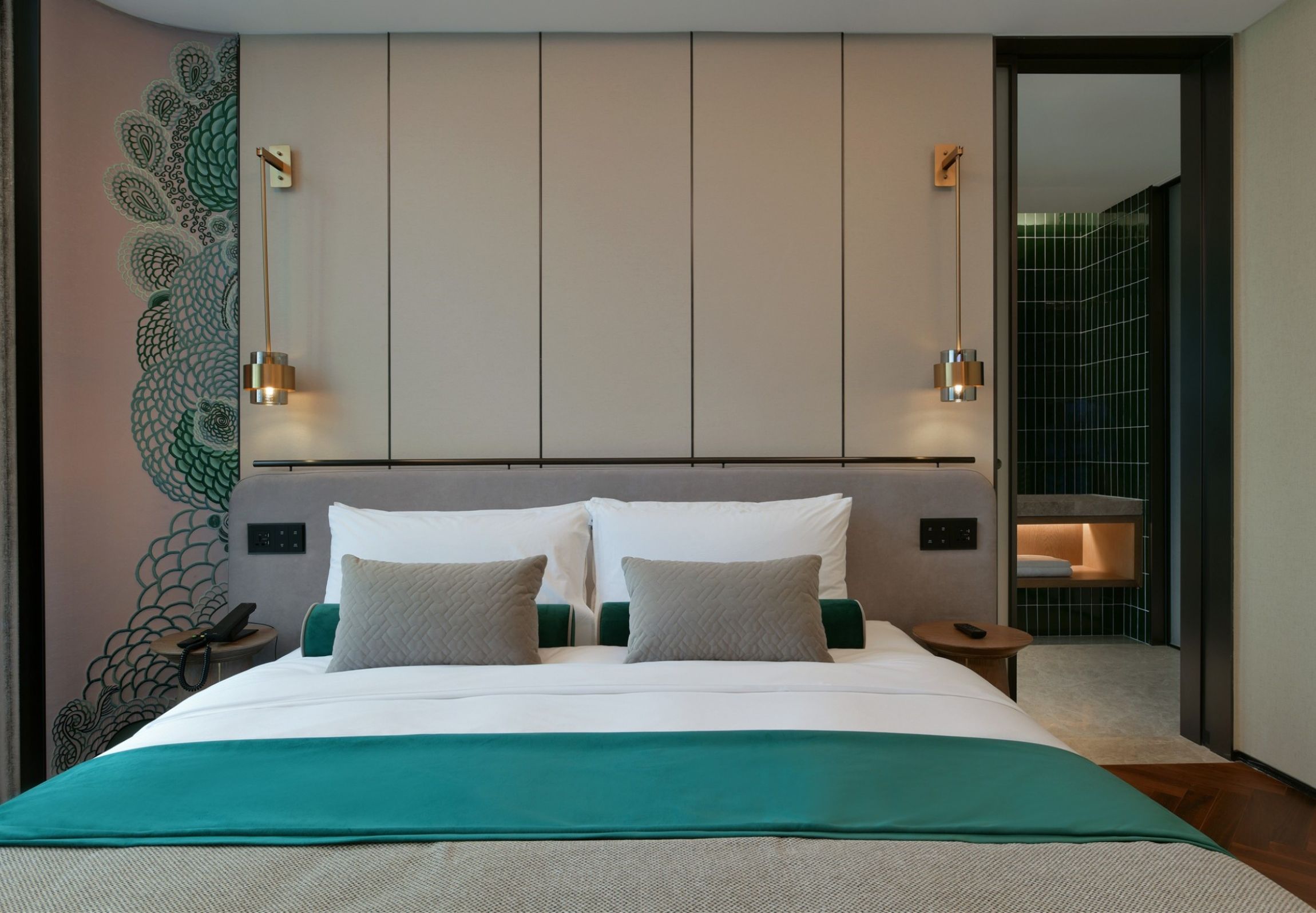 A modern hotel room with a large bed, two bedside tables, a wall-mounted light fixture, and a peacock mural.