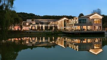 A modern hotel with a reflective pool, multiple buildings, and a forested hill in the background.