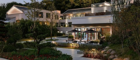 A modern multi-story building with outdoor seating areas, surrounded by landscaped gardens and trees.