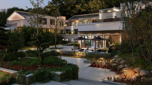 A modern multi-story building with outdoor seating areas, surrounded by landscaped gardens and trees. - Blossom Hill Hotel Nanjing Bojin (Nanjing)