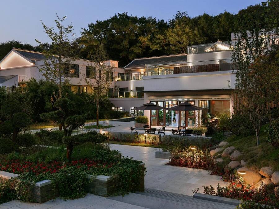 A modern multi-story building with outdoor seating areas, surrounded by landscaped gardens and trees.