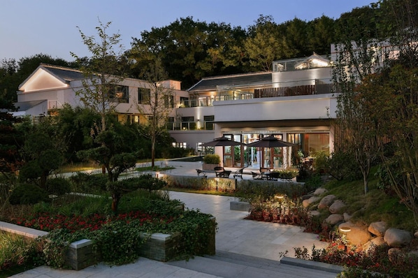 A modern multi-story building with outdoor seating areas, surrounded by landscaped gardens and trees. - Blossom Hill Hotel Nanjing Bojin (Nanjing)