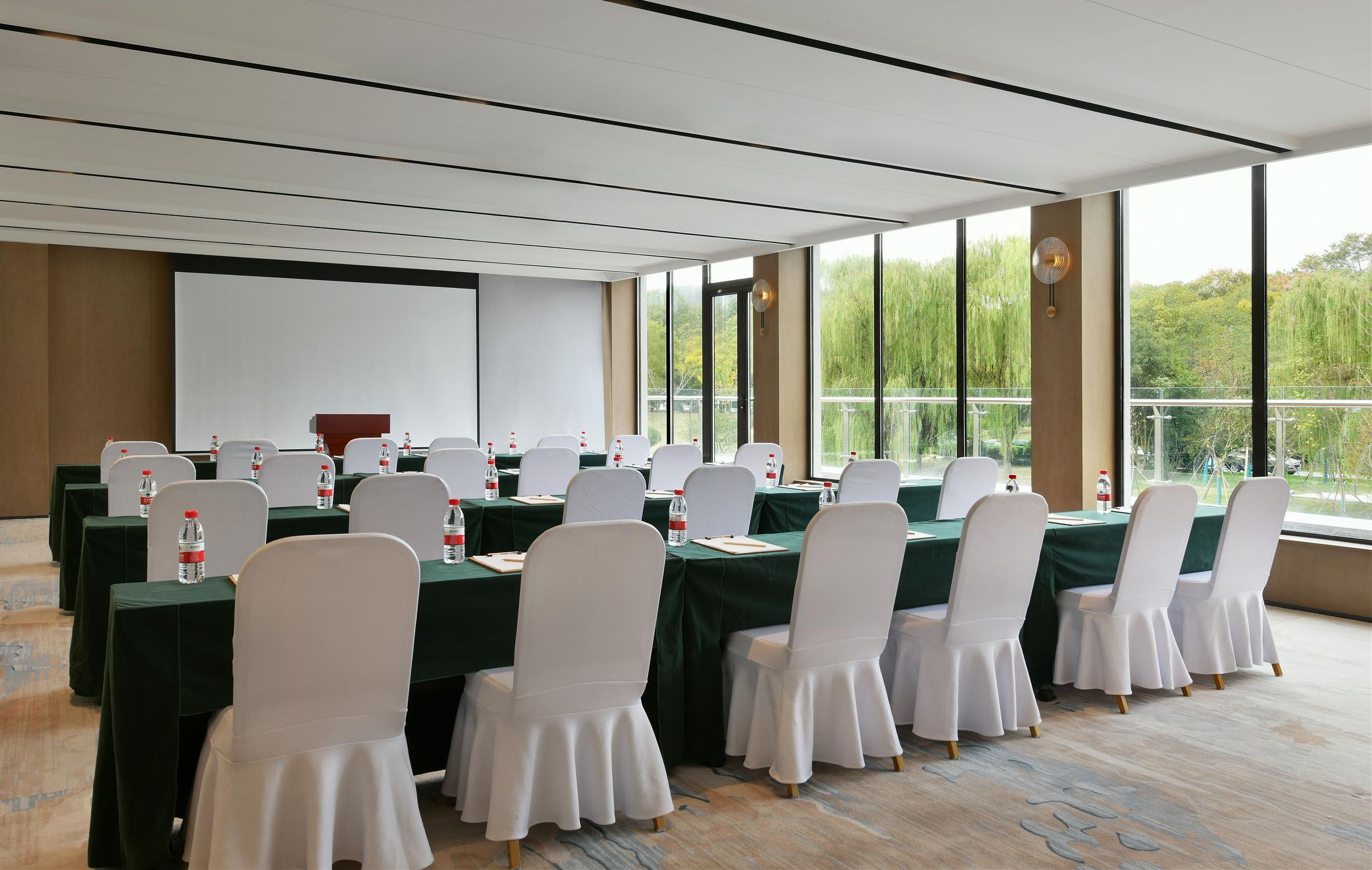 A conference room with tables set for meetings, equipped with water bottles, and large windows offering a view of greenery.