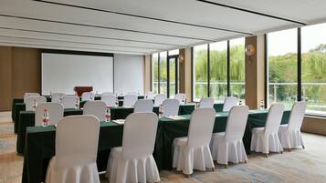 A conference room with tables set for meetings, equipped with water bottles, and large windows offering a view of greenery.