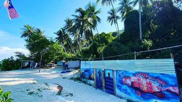 A beach scene with a mural of a fish, palm trees, and a Malaysian flag.