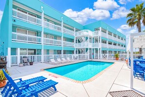 Ein mehrstöckiges Hotel mit Poolbereich, Sitzgelegenheiten im Freien und blauem Himmel.
