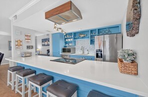 A modern kitchen with a central island, blue cabinetry, stainless steel appliances, and a decorative fish wall art piece.