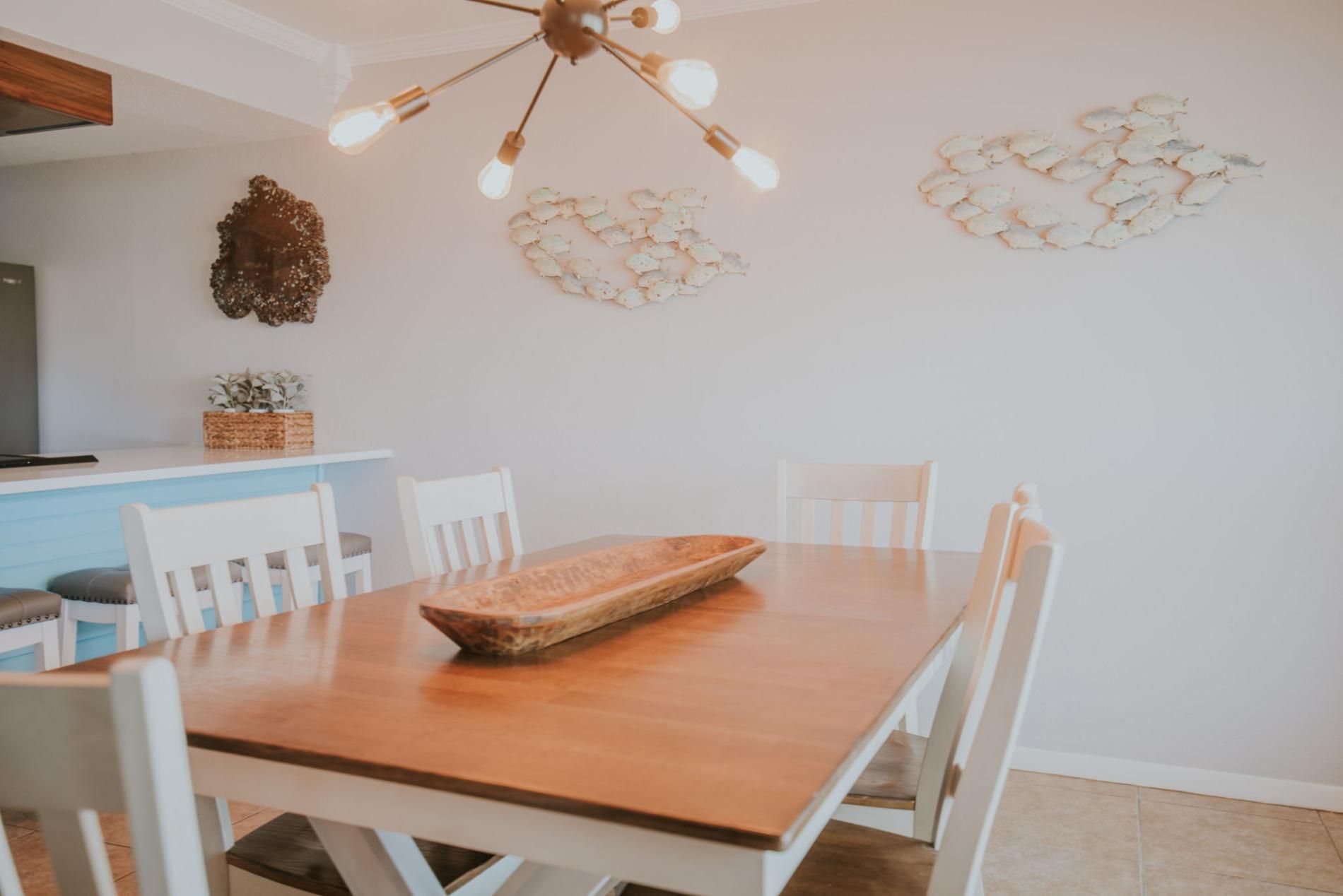 A dining area with a wooden table, white chairs, a decorative wall piece, and a ceiling light fixture.