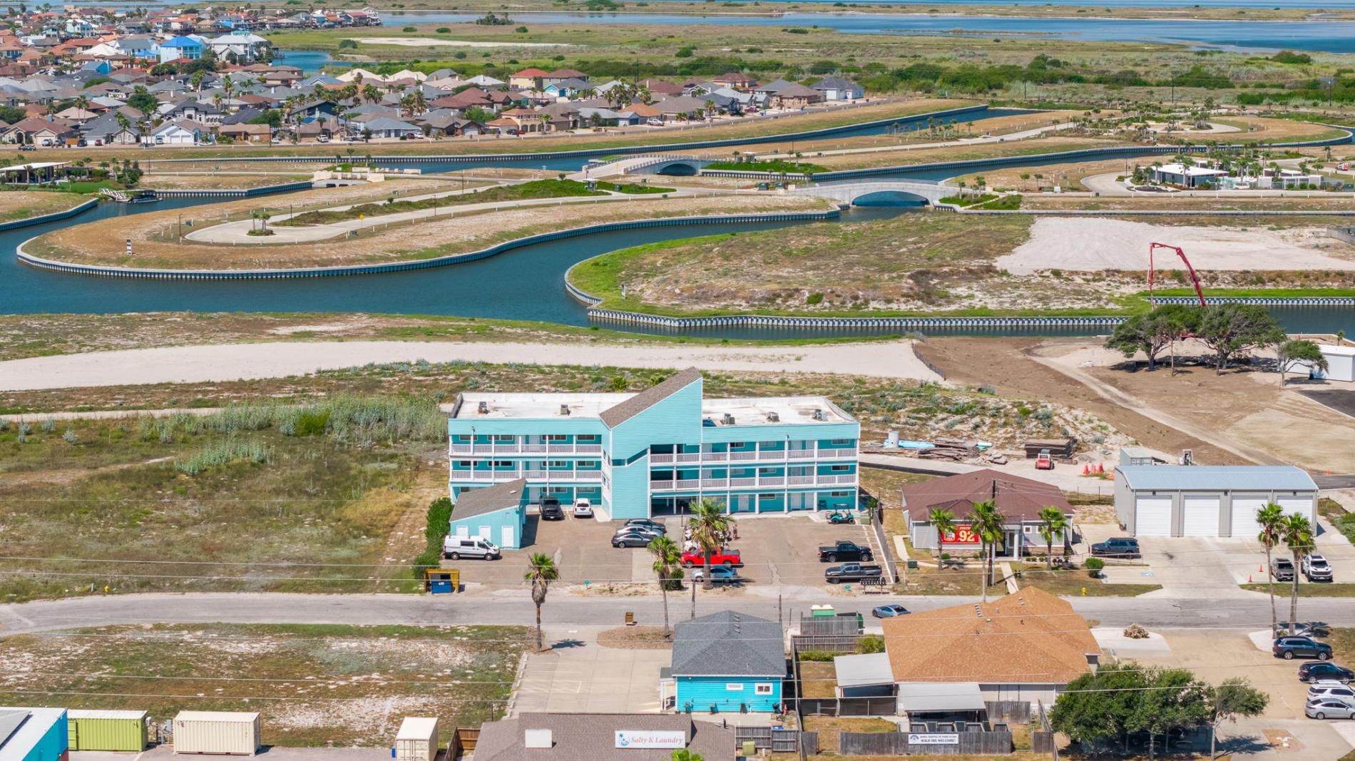 A coastal hotel with a parking lot, a swimming pool, and a view of the ocean.