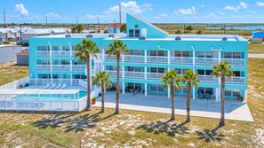 Un bâtiment à deux étages avec une piscine, des palmiers et un ciel dégagé.