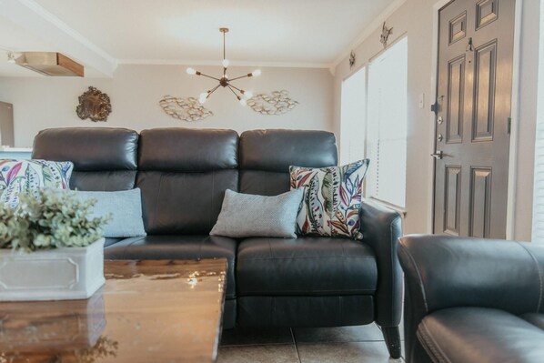 Ein Wohnzimmer mit einem schwarzen Ledersofa, einem Holztisch und einer Deckenleuchte.