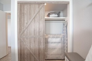 Ein begehbarer Kleiderschrank mit einer Schiebetür im Bauernhausstil, ein Regal mit gefalteter Kleidung und einem gemusterten Vorhang.
