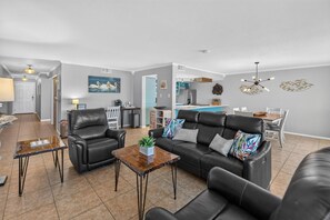 A modern living room with a leather sofa, a coffee table, and a dining area with a kitchen in the background.