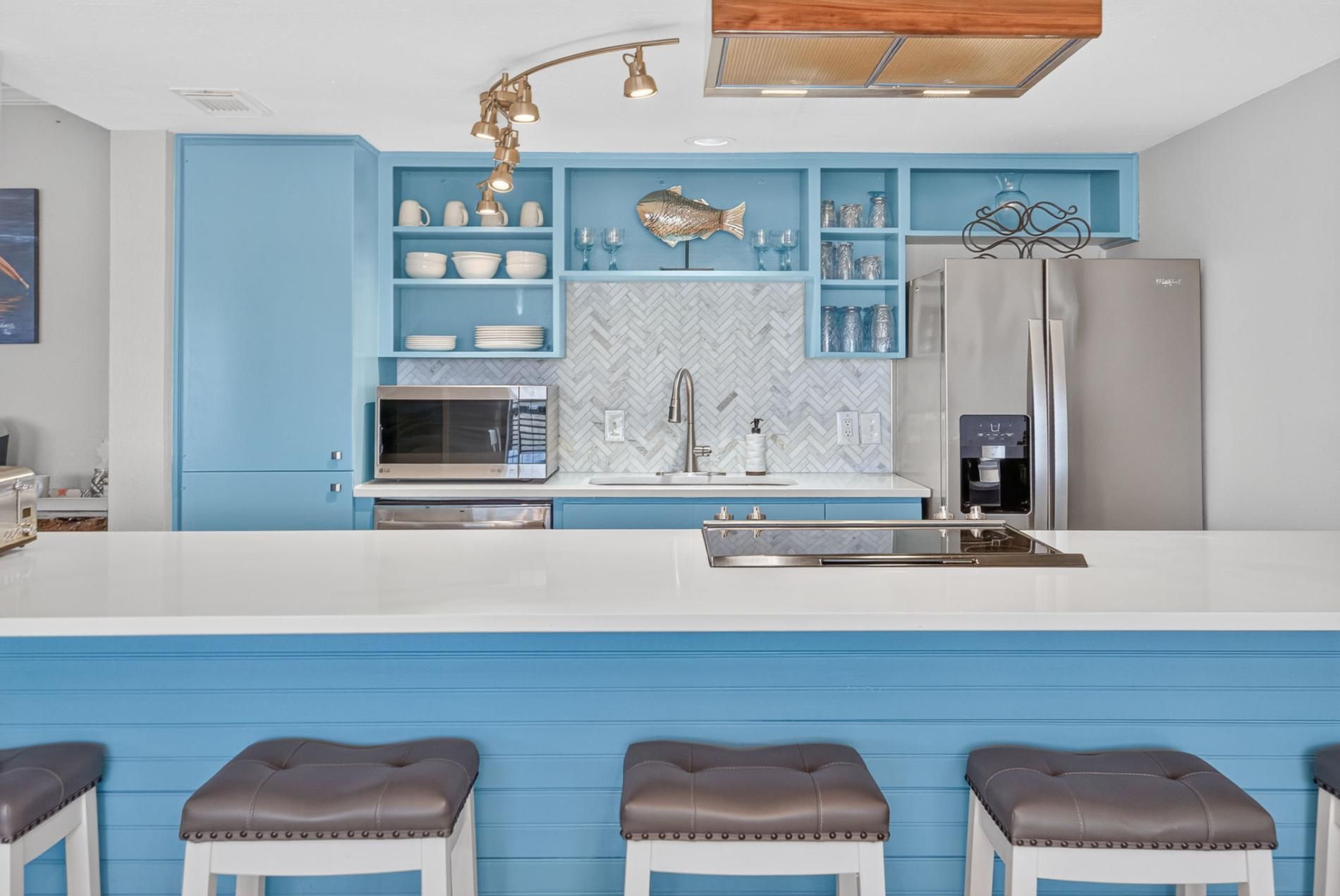 A modern kitchen with a blue color scheme, stainless steel appliances, and a herring fish decoration on the wall.