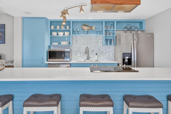 Una cocina moderna con una decoración azul, electrodomésticos de acero inoxidable y un adorno con forma de arenque en la pared.
