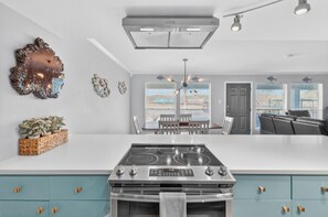 A modern kitchen with a central island, a dining area with a chandelier, and a living room with a sofa.