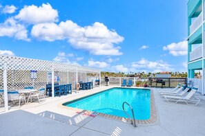 Un espace piscine comprenant des chaises longues, une table de billard et un coin salon abrité.