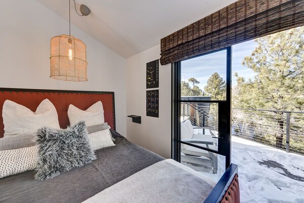 Une chambre avec un grand lit, un luminaire suspendu et une vue sur un balcon extérieur enneigé.