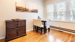 A dining area with a wooden table and chairs, a dark wooden cabinet, and a window with blinds. - Cozy two bedroom close to Wrigley Field (Chicago)