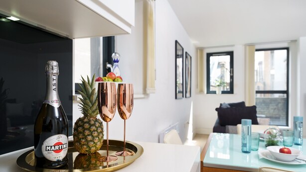 A martini bottle, pineapple, and two copper glasses on a tray in a modern kitchen with a dining area visible in the background.