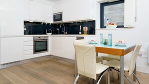 A modern kitchen with white cabinets, a built-in oven, a microwave, and a dining area with a wooden table and chairs.