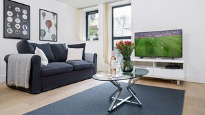 A modern living room with a dark grey sofa, a glass coffee table, a flat-screen TV, and framed artwork on the wall.