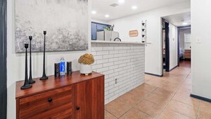 Un corridoio con parete in mattoni bianchi, un armadietto in legno con oggetti decorativi e una zona cucina sullo sfondo.
