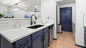 Una cucina moderna con ripiani bianchi, mobili scuri, un rubinetto nero e una porta blu.