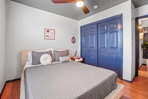 Een slaapkamer met een bed, een plafondventilator, een blauwe deur en een klein nachtkastje met een lamp.