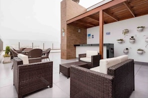 Une terrasse sur le toit aménagée avec des meubles en osier, des plantes en pot et un téléviseur à écran plat.