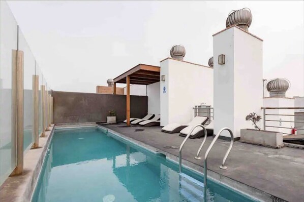 Une piscine sur le toit, dotée de chaises longues et d’une pergola.