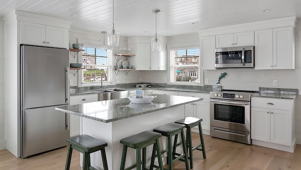 Una cocina moderna con armarios blancos, electrodomésticos de acero inoxidable y una isla grande con taburetes de bar.