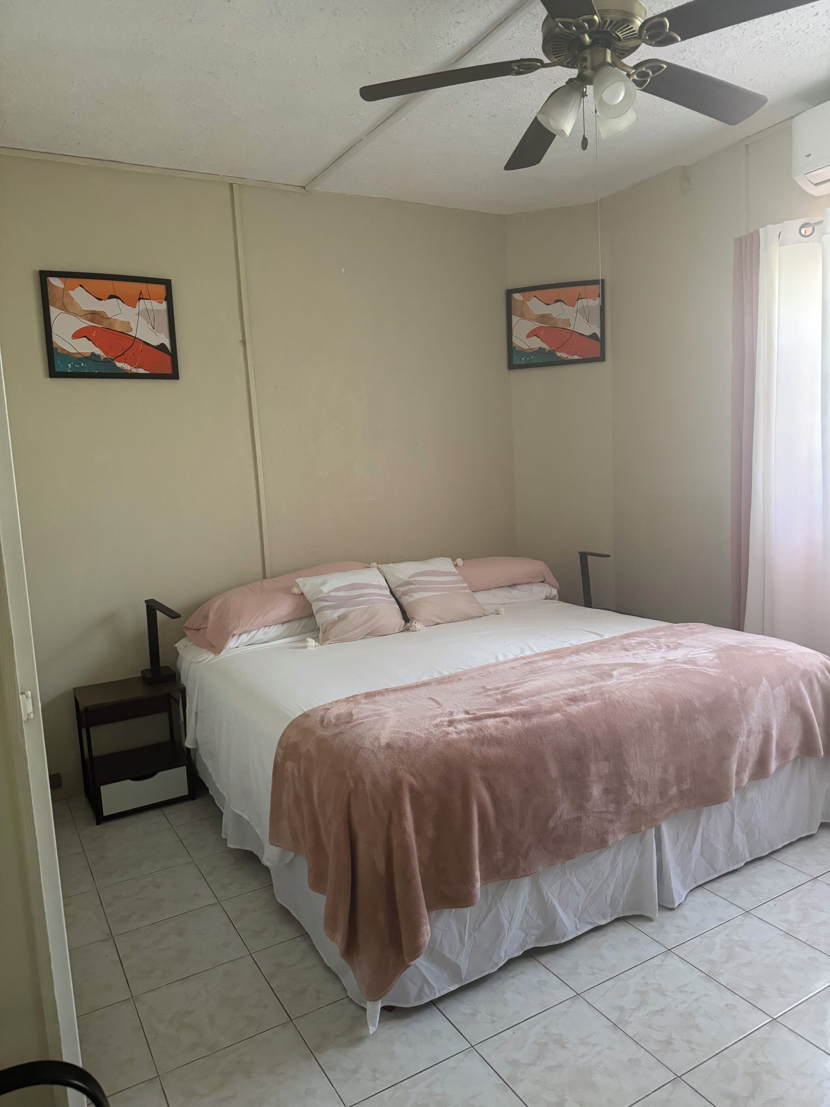 Une chambre à coucher avec un lit, un ventilateur de plafond et deux tableaux accrochés au mur.
