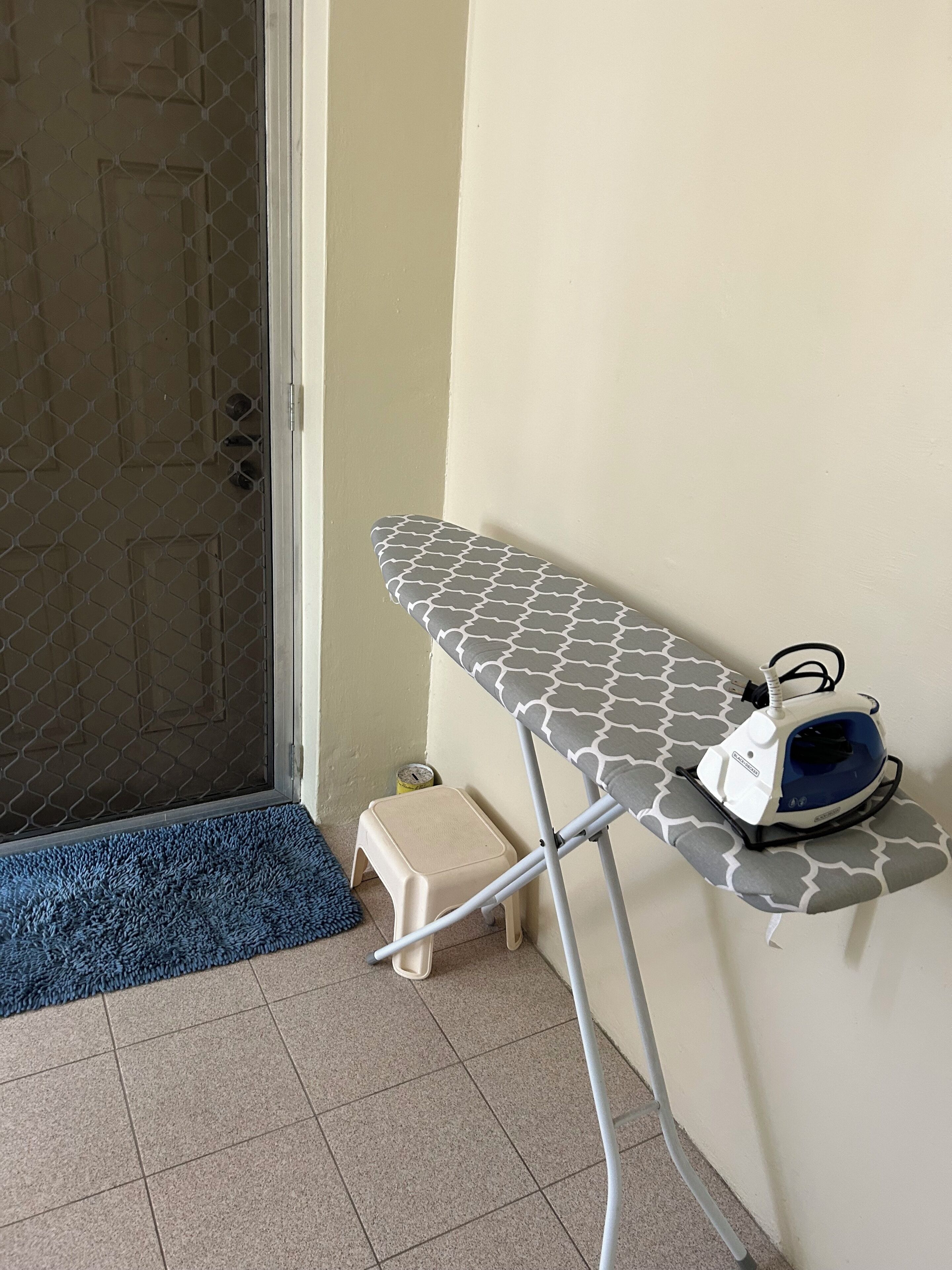 Un rincón con una tabla de planchar, un planchador y un taburete pequeño.