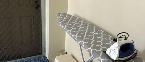 Un rincón con una tabla de planchar, un planchador y un taburete pequeño.