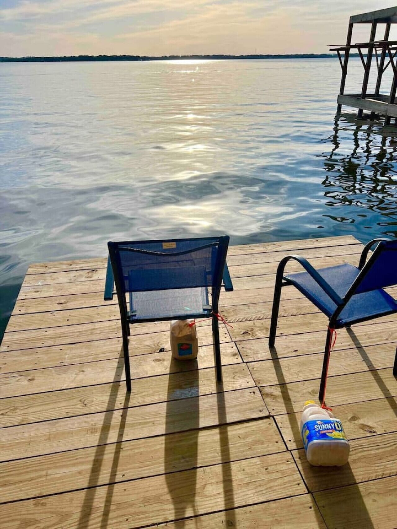 Eine Holzsteg mit zwei blauen Stühlen und einer Flasche Sunny Delight auf dem Deck.