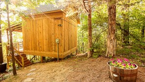 Una cabaña de madera con un balcón y escaleras que llevan a ella, rodeada de árboles y un jardín de flores.