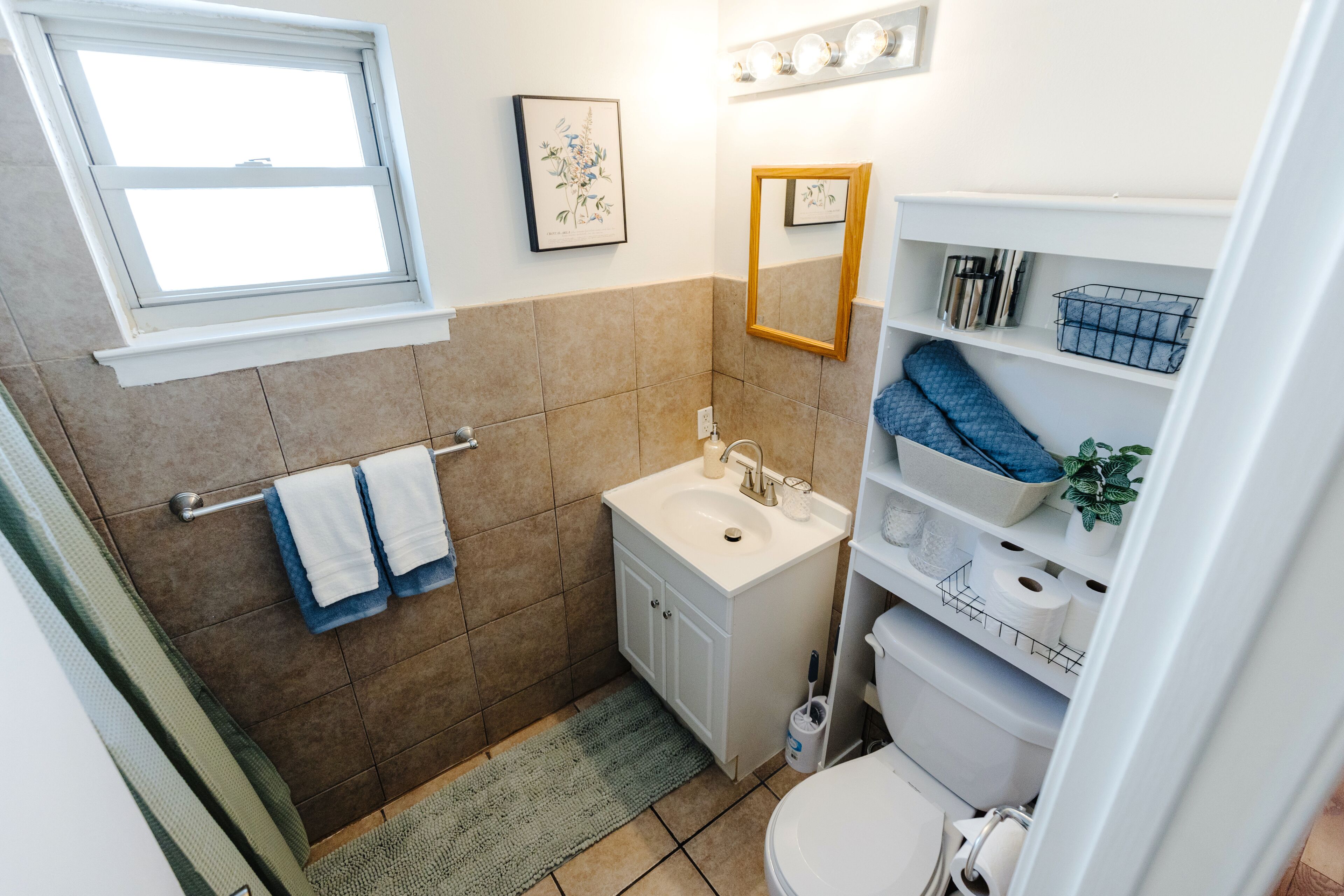Une petite salle de bain avec une fenêtre, un lavabo, un miroir et des étagères contenant des articles de toilette.